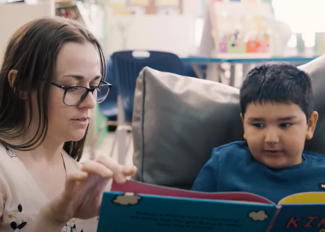 Teacher reading to a young Indigenous child holding a book with the title: "Good Night Stories for Rebel Girls."