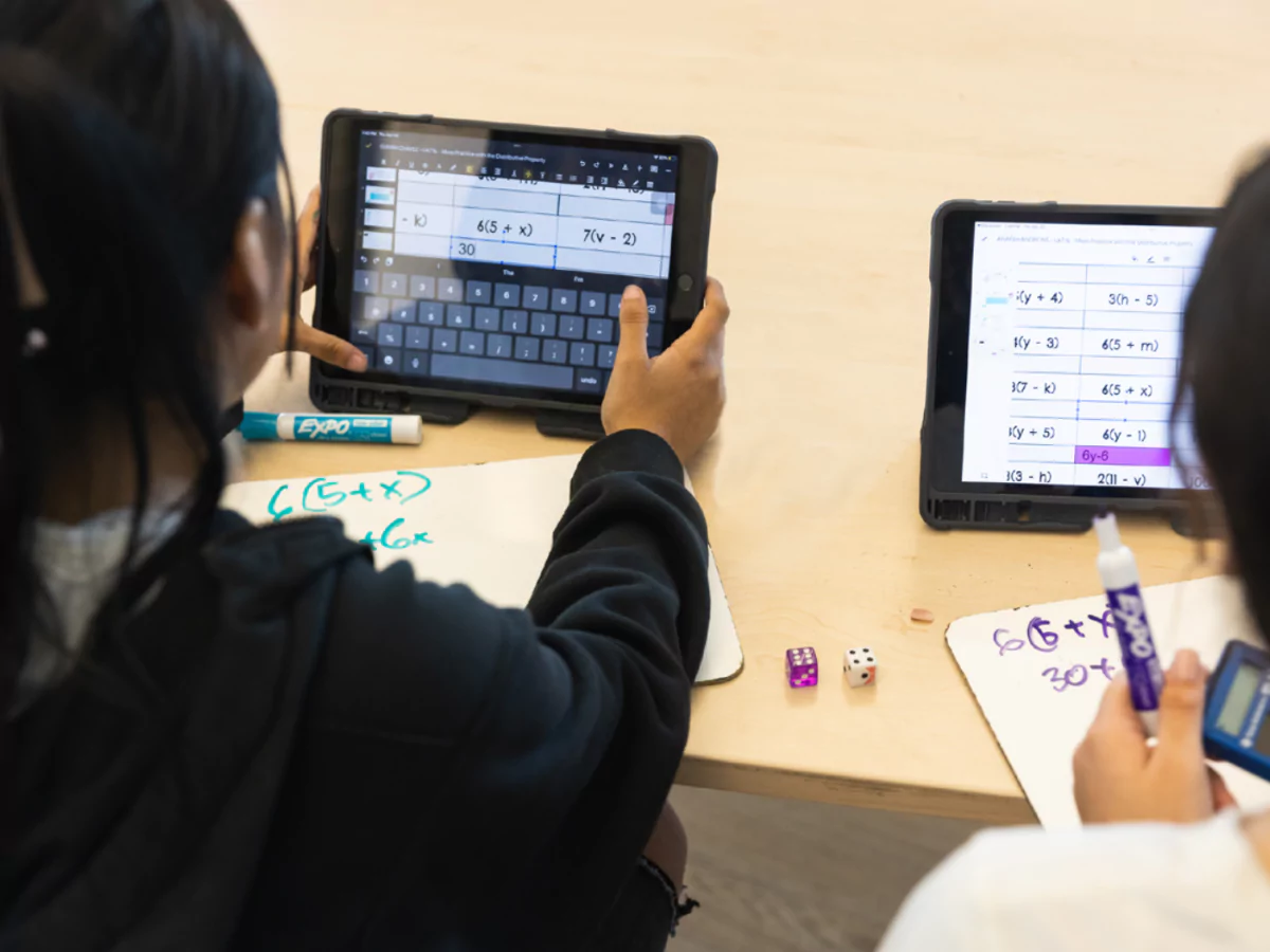 Students copying math equations from tablets onto individual whiteboards. 