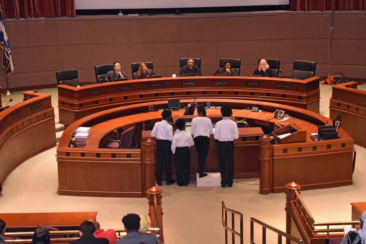 A group of middle school students standing in front the Judge's bench, presenting to the panel of 5 judges that sit in front of them.