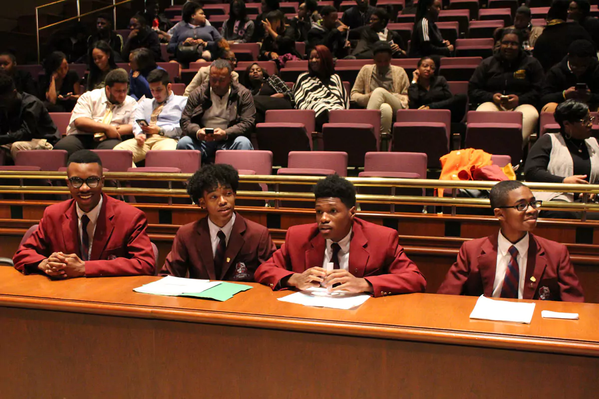 A group of middle school students wearing burgundy suits sitting at either the Defendant's Table or the Plaintiff's Table. 